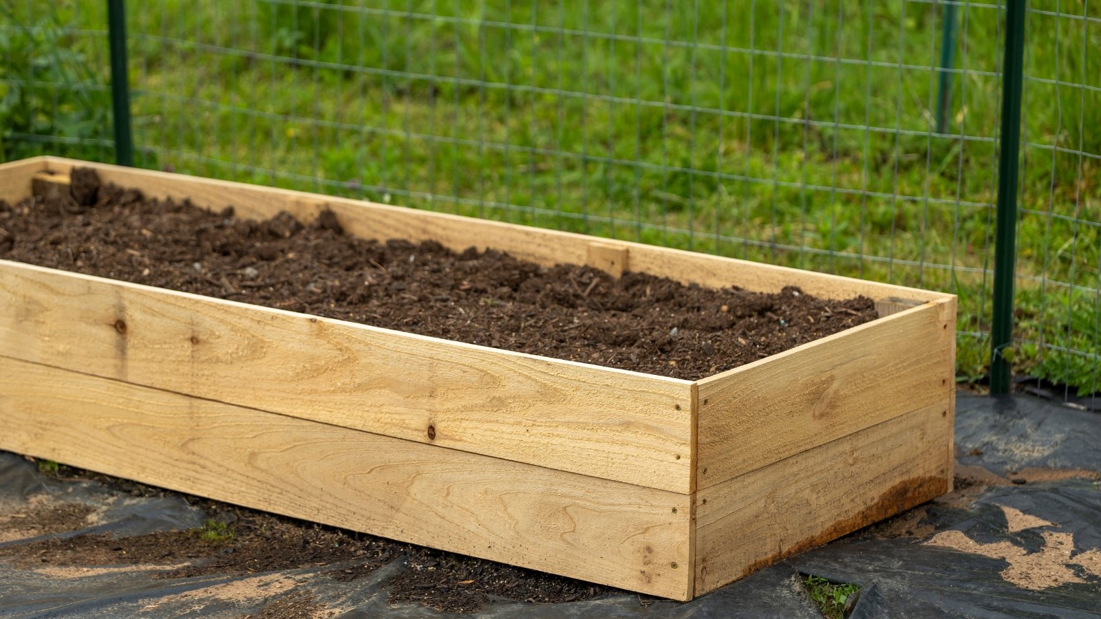 A close-up of a wooden raised garden bed filled with loose, dark brown soil.